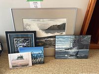 Set of two framed landscape pictures, two smaller unframed landscape pictures, and one card shown together on carpeted floor near wooden furniture