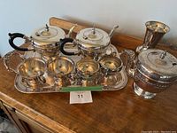 Full view of silver coffee and tea set on wooden surface including teapots, creamers, sugar bowl, and tray