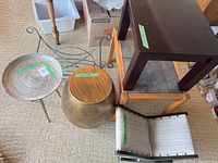 Overview of the lot showing the metal spiral top tripod table, wooden drum table, rectangular brown wooden table, and wrought iron rocker footstool.