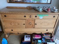Front view of large solid oak sideboard showing carved drawer fronts and dark round metal pulls, with various teacups and books around it.