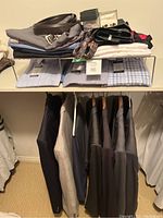 Five men's suit jackets hanging with three folded dress shirts on shelf above, displaying clothing included in the lot.
