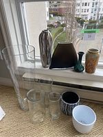Wide angle view showing all items on windowsill and floor near window - a collection of glass vases, ceramic pots, and metal vase.