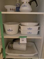 Shelf view showing multiple CorningWare items including large casserole, rectangular baking dishes, coffee percolator, and a mixing bowl with distinct pattern