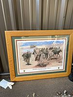 Full view of framed lithograph showing military scene with soldiers, horses and helicopter, oak-colored wood frame and green double matting.