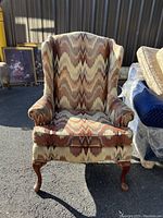 Front view of wingback chair showing patterned fabric upholstery and wooden legs in outdoor lighting.