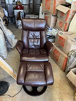 Full view of chair and ottoman set in storage area with brown leather upholstery and swivel bases.