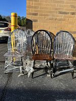 Six Windsor style dining chairs with black spindles and legs and dark brown seats, wrapped in clear plastic, showing some scratches and wear.