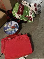 Photo showing red and green Christmas blankets with snowflakes and poinsettias, a red quilt or throw, and a round holiday tin with children and tree scene.