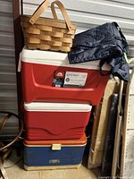 Stack of three coolers with a picnic basket on top along with a dark bag or cloth.