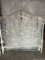 White and brass iron headboard wrapped in plastic.