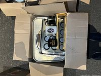 Photo showing cardboard box with metal baking pans, glass mixing bowls, coffee mugs and wooden tray