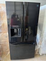 Front view of black French door refrigerator with bottom freezer and water/ice dispenser