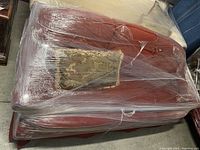 Top-down photo of red upholstered sofa wrapped in plastic with decorative throw pillow on seat