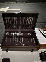 Open wooden flatware box showing rows of dinner knives, forks, and spoons in French Scroll pattern