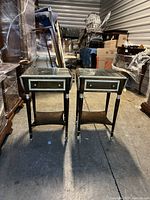Front view of identical pair of dark wood side tables with white trim and glass tops with drop sides in storage unit.