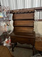 Full front view of vintage wooden hutch showing upper shelving, decorative crest and lower drawer