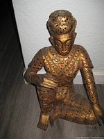 Front view of seated wooden statue of a man, showing jewel decorations and gold paint.