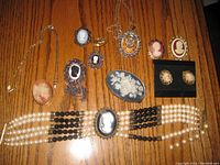Full view of all 11 cameo jewelry pieces arranged on wood surface, showing necklaces, brooches, earrings, choker, and belt buckle.