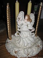Full front view of the porcelain angel figurine seated on a decorated base with four candles around it.