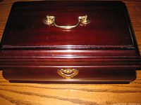 Closed view showing dark mahogany wood polished finish and brass handle and lock plate on front.