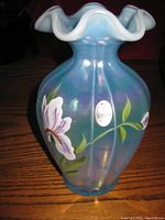 Front view of the 7-inch tall blue iridescent Fenton vase with white floral hand-painted design and original Fenton label sticker visible.