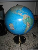 Daylight photo of the globe showing the world map with Americas in view, mounted on a metal base with power cord.