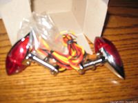 Pair of bullet-shaped Harley Davidson motorcycle lights with red lenses and chrome housing along with attached wiring, set displayed out of box.