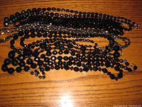 Top view of seven jet black beaded necklaces piled together showing variety of bead sizes and styles.