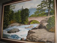 Framed oil on canvas painting showing a detailed river with rocks, trees and mountains in background, signed bottom right.