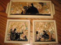 Three framed vintage silhouette pictures displayed on wooden surface, showing woman in historical domestic scenes.