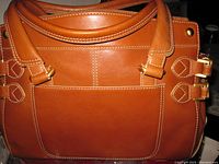 Front side view of tan leather purse with a large exterior pocket and double strap details with gold rivets.