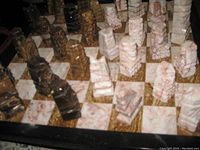 Angle view of chessboard with both light and dark geometric chess pieces arranged on squares, showing unique sculpted design and stone patterns.