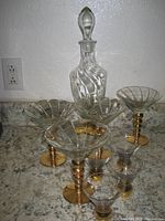 Full set of the vintage glass decanter and eight matching glasses on countertop, showing gold trim and swirl pattern