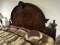 Front angled view of king size cherry wood headboard showing arched top and intricate scroll and floral carvings