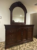 Front view of large dark wooden dresser with three drawer columns and middle double cabinet doors. Carved scroll work details visible on top edge and around doors.