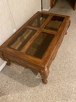 Angle view of the carved coffee table showing wood engraved legs and four glass top panels.