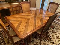 Photo of rectangular wooden dining table with geometric patterned top and six matching wooden chairs with woven backs in dining room setting