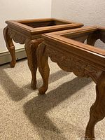 Two wood end tables with glass tops and detailed carved scroll work on legs and aprons shown side by side.