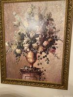 Photo of an oil painting depicting a floral bouquet in a gold vase atop a pedestal, framed in an ornate gold frame.