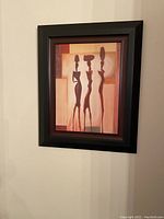 Photo of framed Art Deco style picture with three stylized dancing women in silhouette in warm tones.