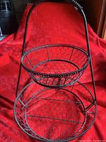 Front view of two-tier wire basket rack showing oval handle and bowl-shaped top tier over larger bottom tier