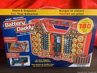 Photo of original Battery Daddy packaging showing the product, its double-sided design, capacity for 180 batteries, and built-in battery tester function.