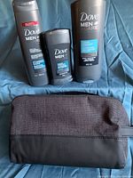 Dove Men+Care grooming products and toiletry bag arranged on blue fabric background. Includes body wash, deodorant, shampoo and bag.