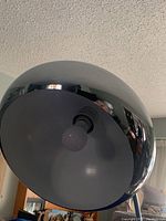 Close-up of the chrome floor lamp's shade interior, showing the single bulb and matte inner surface.