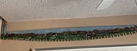 Full length view of the 6-foot two-man saw mounted on wall showing detailed hand painting of rural landscape scene along the blade.