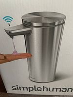 Photo of the stainless steel sensor liquid soap dispenser showing soap dispensing onto hand and wireless sensor symbol.