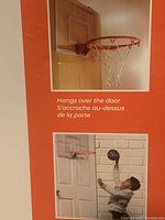 Photo showing mini basketball hoop with clear shatterproof backboard hanging over door, orange rim, white net, in use by child.