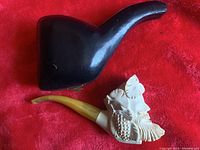 Photo showing pipe with carved bust and black latched case on red background