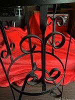 Close-up view of the black wrought iron material showing curled scroll designs and stable circular base on a red blanket background.