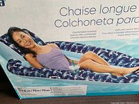 Photo of woman reclining on blue inflatable lounger with white palm tree print and curved padded headrest.